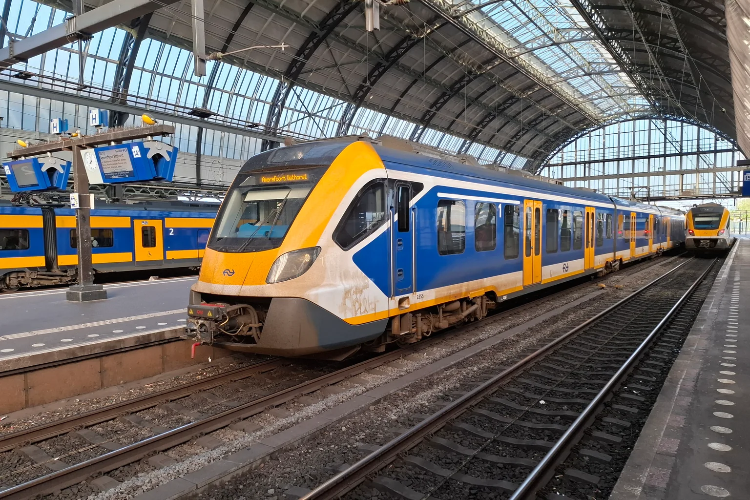 Een geel-blauwe NS-Sprinter aan het perron onder de overkapping van Amsterdam Centraal in mei 2024